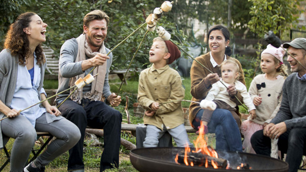 Zwei Familien sitzen zusammen um ein Lagerfeuer und rösten Marshmellows.