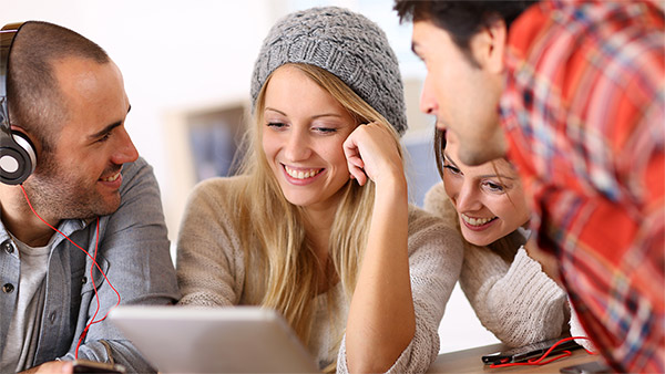 Vier Studentinnen und Studenten sehen sich auf einem Tablet etwas an.