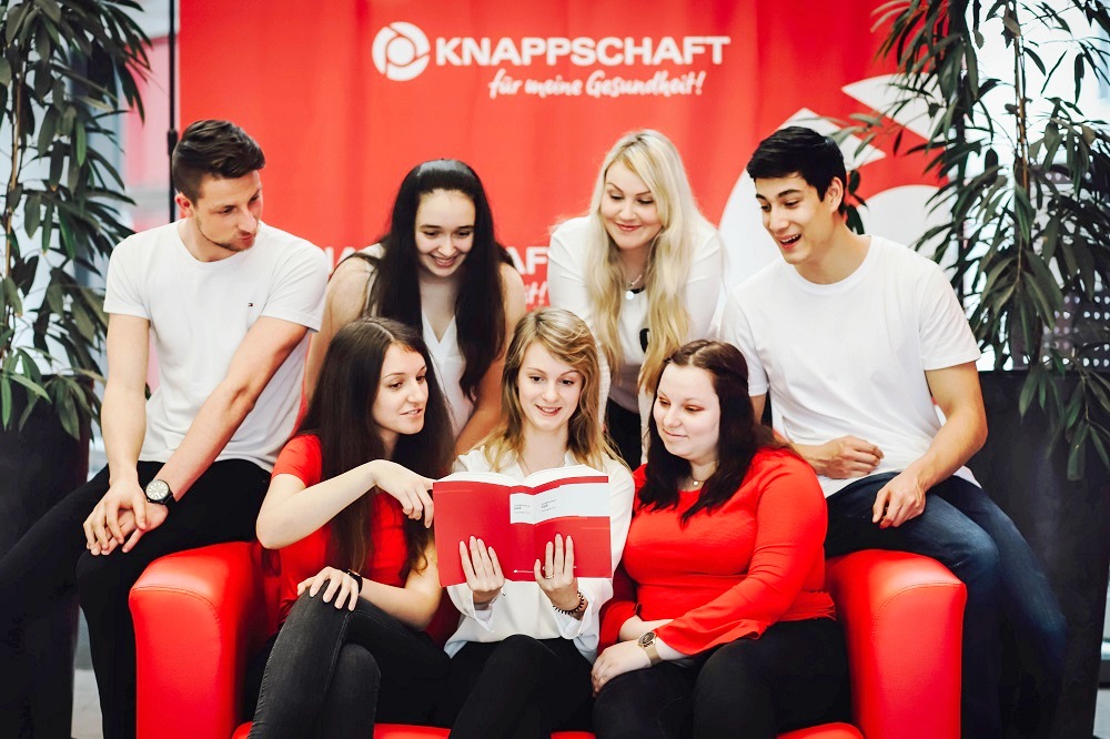 Eine Gruppe von Auszubildenden, jungen Frauen und Männern, steht um einen Tisch mit Lehrbüchern. Eine Gruppe von Auszubildenden, jungen Frauen und Männern, steht um einen Tisch mit Lehrbüchern.