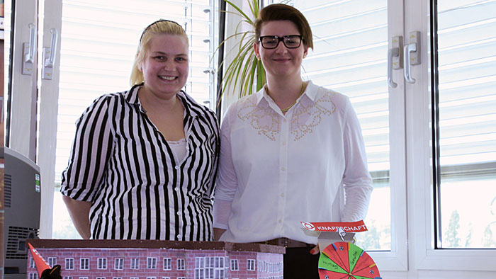 Zwei Auszubildende stehen lächelnd vor dem aus Pappe gebastelten Modell des Gebäudes ihrer Regionaldirektion.   Zwei Auszubildende stehen lächelnd vor dem aus Pappe gebastelten Modell des Gebäudes ihrer Regionaldirektion.