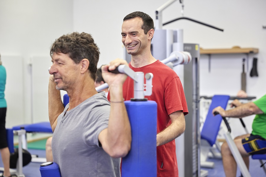 Ein Patient wird im modernen MTT-Raum von einem Therapeuten an einem Trainingsgerät betreut. Ein Patient wird im modernen MTT-Raum von einem Therapeuten an einem Trainingsgerät betreut.