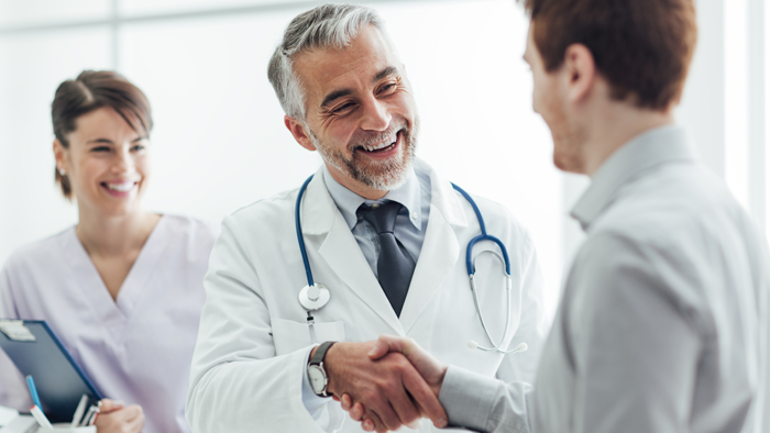 Ein Arzt gibt einem Patienten die Hand. Eine Krankenschwester ist ebenfalls anwesend.