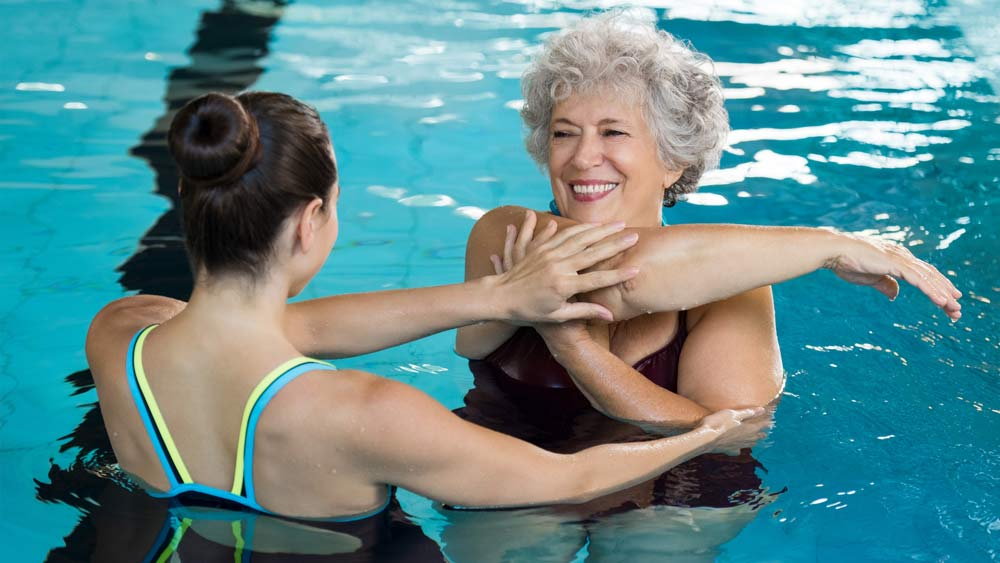 Reha-Patientin mit einer Physiotherapeutin bei der Wassergymnastik.