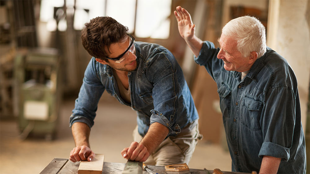 Ein junger Mann und ein alter Mann arbeiten gemeinsam in einer Werkstatt. Ein junger Mann und ein alter Mann arbeiten gemeinsam in einer Werkstatt.