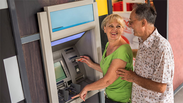 Eine Frau und ein älterer Mann stehen vor einen Bankautomat. Eine Frau und ein älterer Mann stehen vor einen Bankautomat.