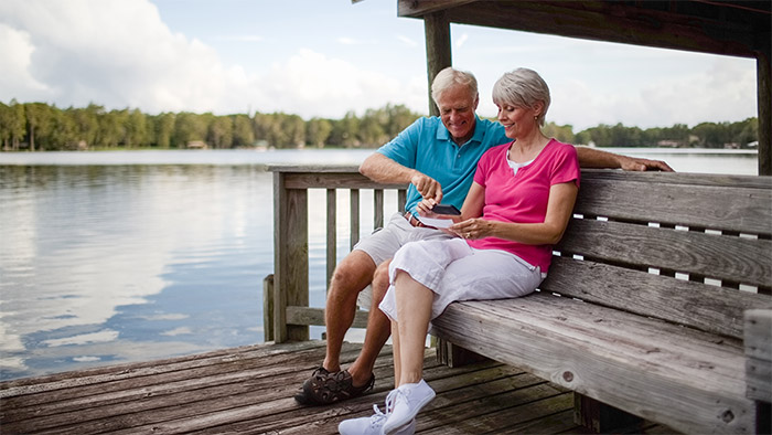 Ein älteres Pärchen sitzt auf einer Bank am See und fotografiert etwas mit einen Smartphone ab. Ein älteres Pärchen sitzt auf einer Bank am See und fotografiert etwas mit einen Smartphone ab.