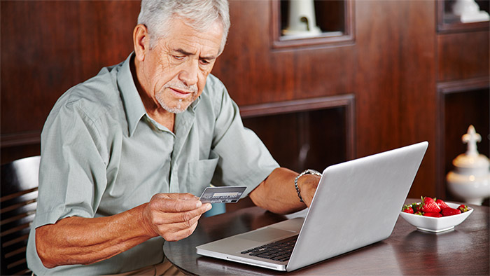 Ein älterer Mann sitzt vor einen Laptop und schaut auf eine Bankkarte.