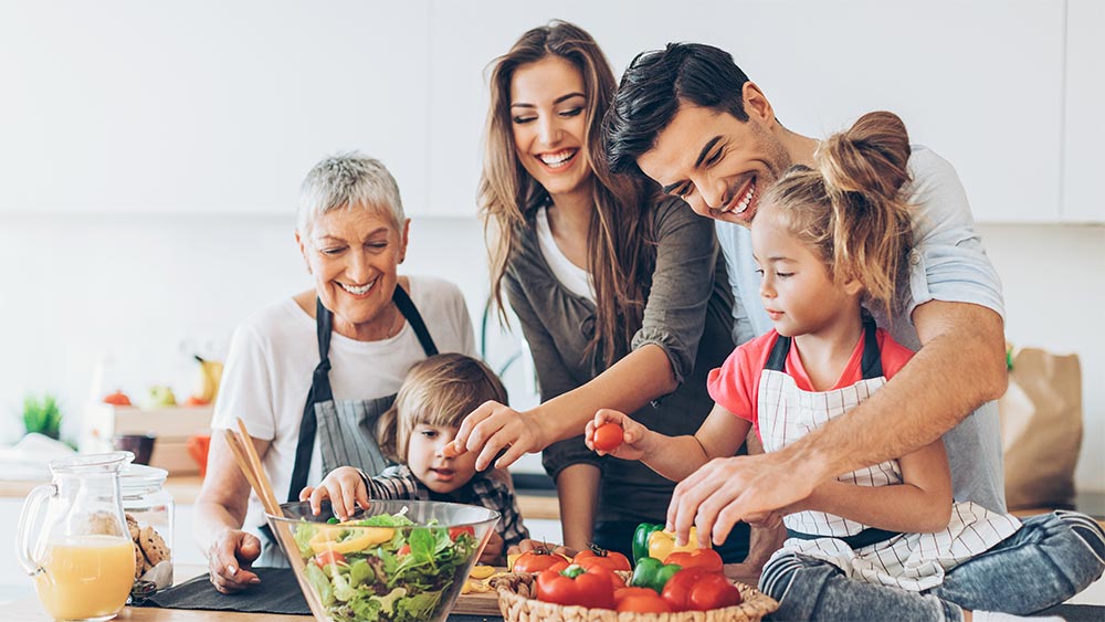 Eine junge Familie mit Großmutter bereiten gemeinsam einen Salat zu.