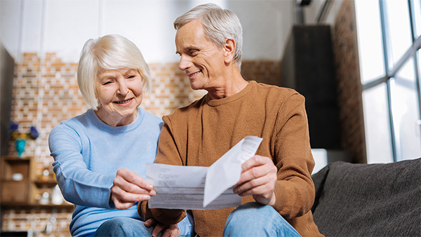 Ein Rentner-Paar sitzt auf einem Sofa und liest gemeinsam ein Papierdokument.