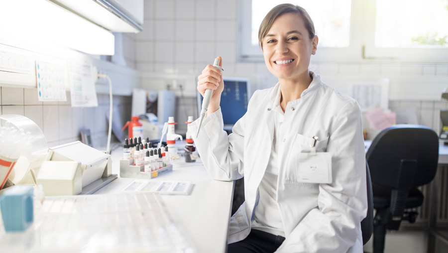 Eine Labormitarbeiterin sitzt mit einer Pipette in der Hand im Labor.