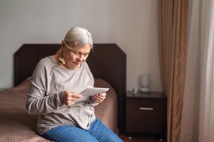 Eine ältere Dame sitzt auf einem Bett und liest einen Brief. 
