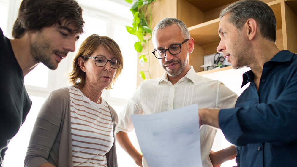 Drei Männer und eine Frau sehen sich ein Papierdokument an. Drei Männer und eine Frau sehen sich ein Papierdokument an.