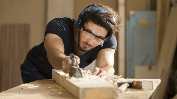 Ein Tischler bearbeitet Holz an einer Werkbank. Ein Tischler bearbeitet Holz an einer Werkbank.